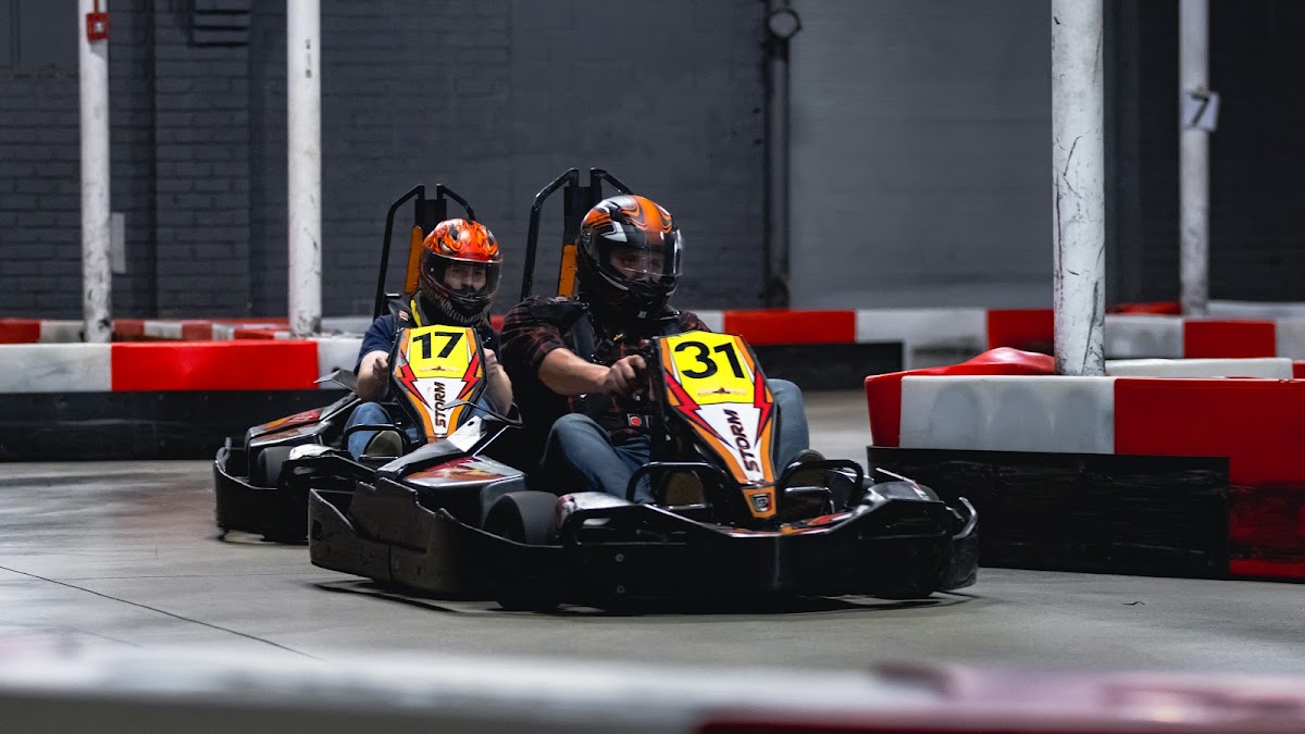 Two drivers in helmets racing rental karts on an indoor track